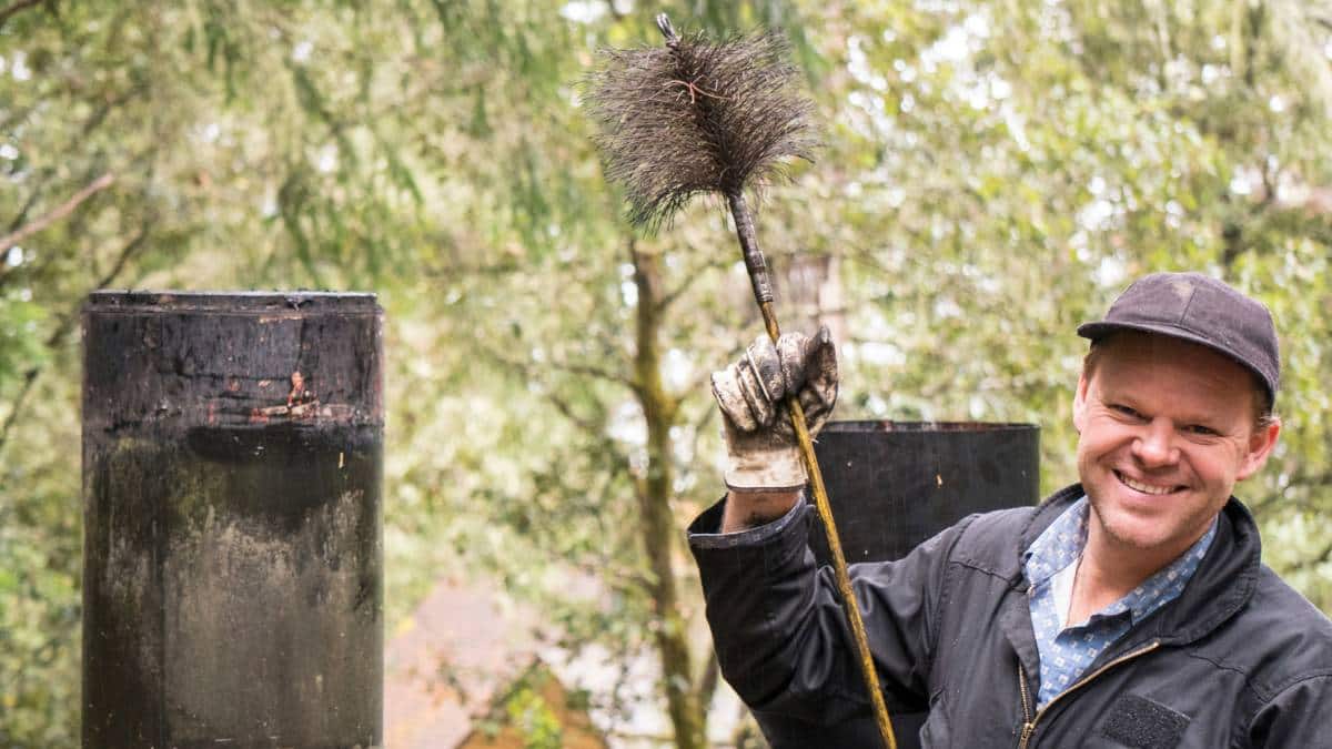 Een professionele schoorsteenveger houdt een borstel vast en lacht. 