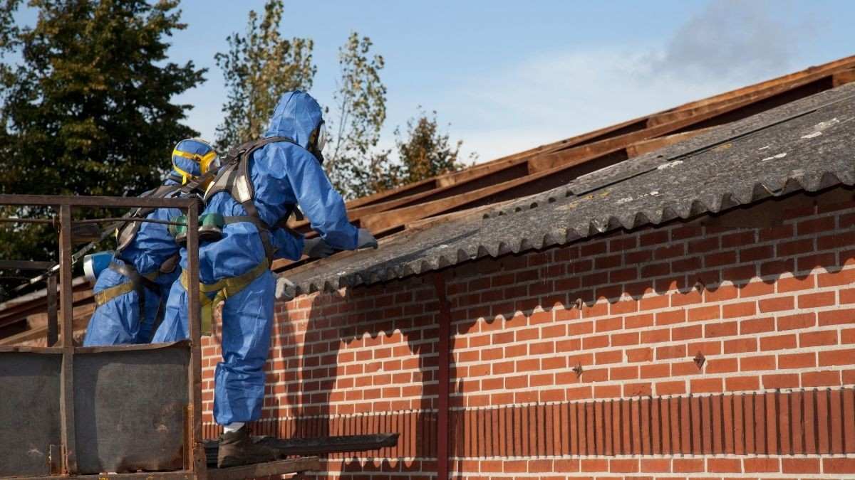 Asbest dak herkennen en verwijderen door specialisten in blauwe beschermkledij die golfplaten van een dak saneren
