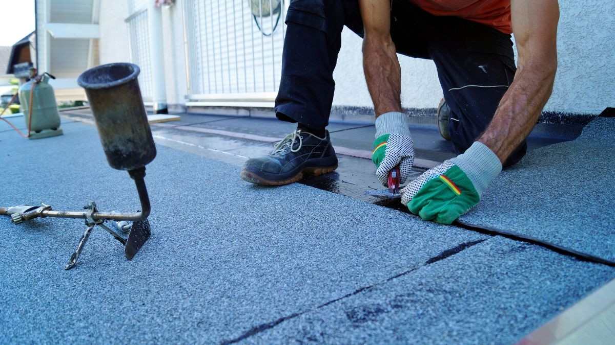 Dakwerker brengt bitumen roofing aan met een gasbrander op een plat dak, de naden worden waterdicht afgewerkt