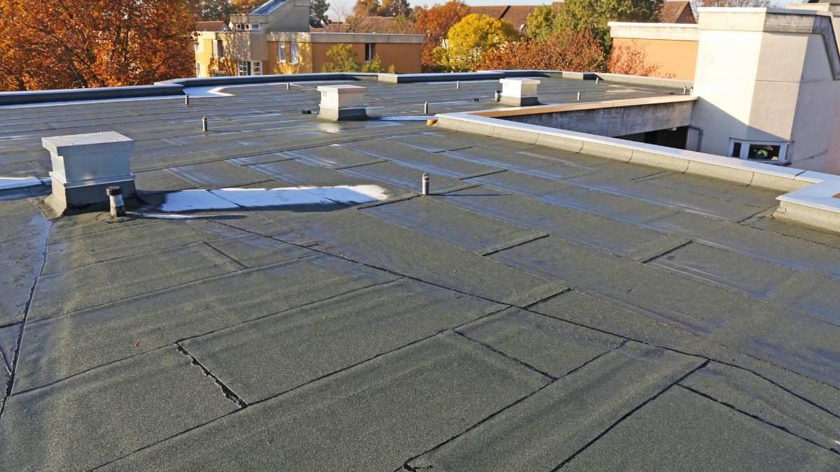 Bovenaanzicht van een plat dak met bitumen dakbedekking, meerdere dakdoorvoeringen en ontluchtingspijpen zijn zichtbaar
