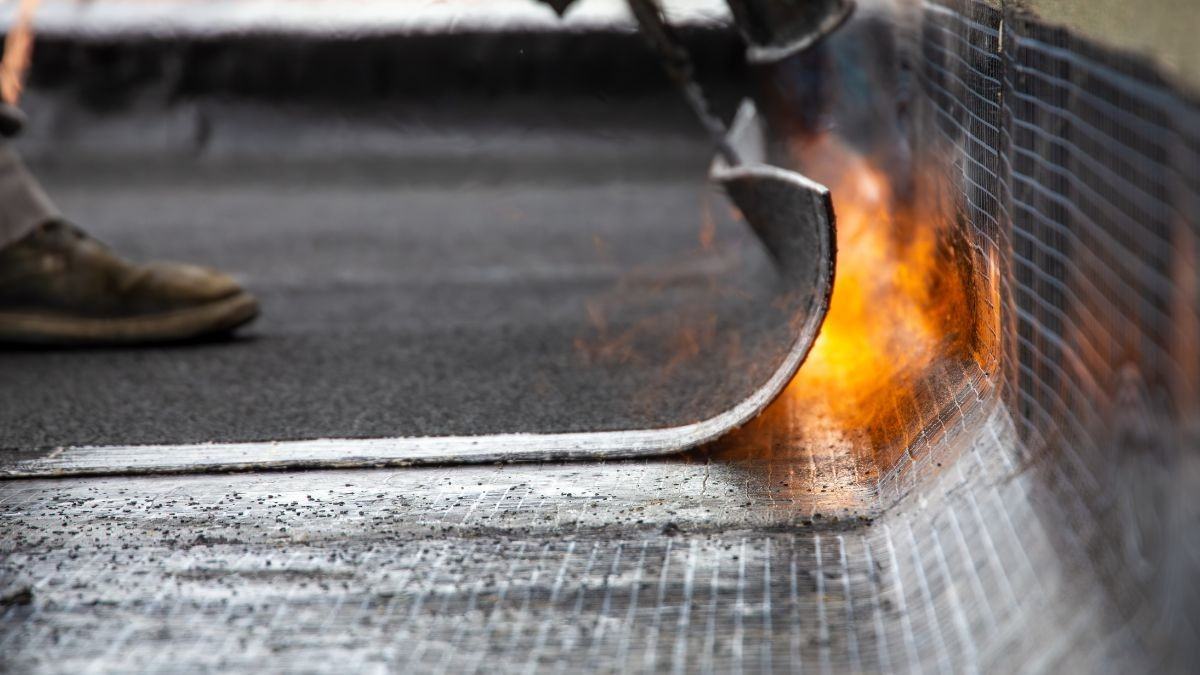 Detail van roofing herstellen bij een dakrand waar een brander de bitumen dakbedekking waterdicht vastsmelt