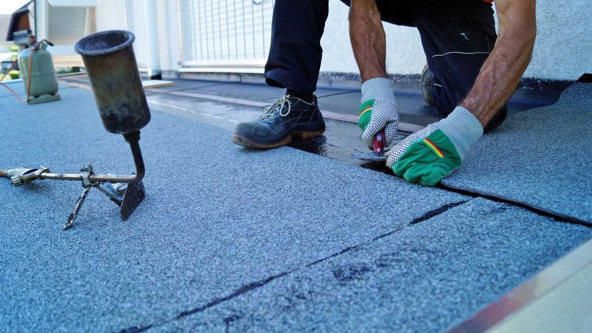 Dakwerker brandt bitumen roofing vast op een plat dak met een gasbrander tijdens het vernieuwen van de dakbedekking