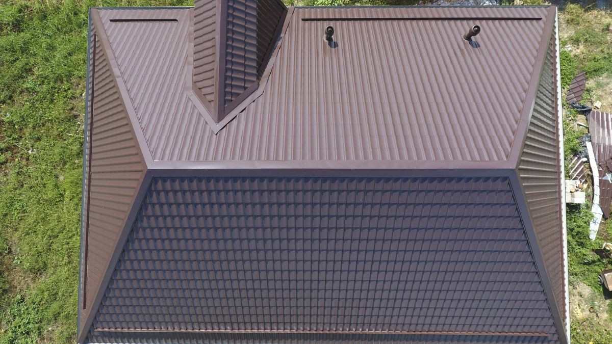 Bovenaanzicht van een dak met vier hellende dakvlakken, een kleine dakkapel en bruine metalen dakpannen