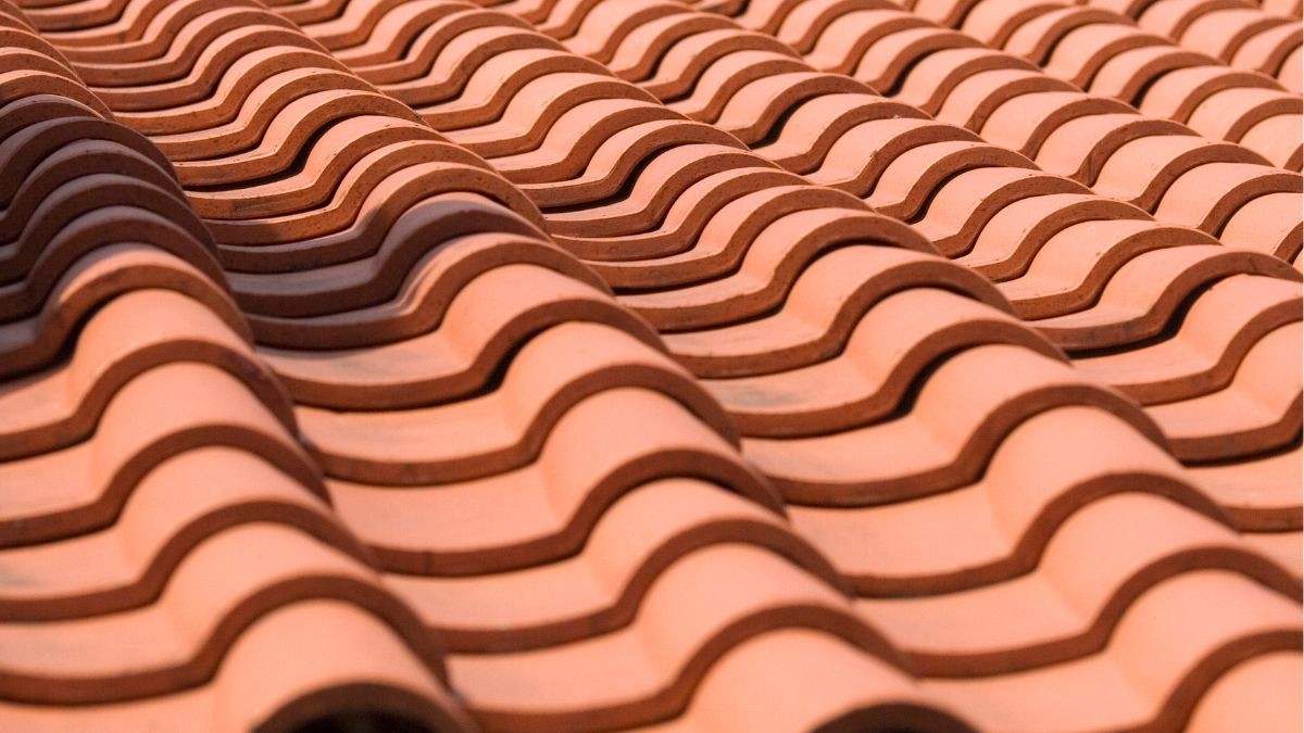 Close-up van oranje holle keramische dakpannen in een golvend patroon, typisch voor traditionele soorten dakpannen in België