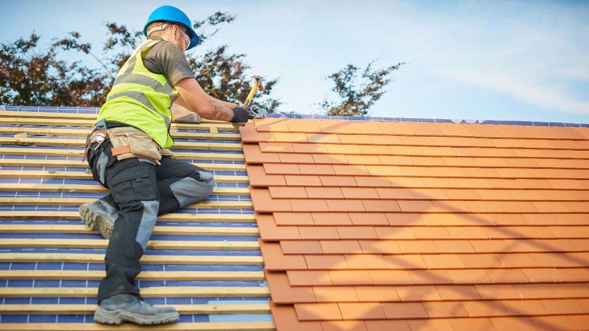 Dakdekker met veiligheidshelm bevestigt vlakke pannen op houten panlatten bij een nieuwbouwproject met hellend dak