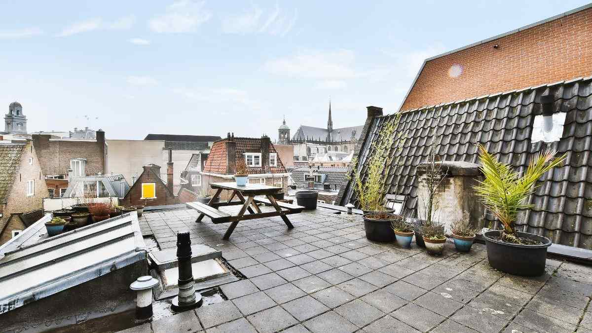 Ruim dakterras aanleggen met betontegels en een houten picknicktafel op een plat dak met uitzicht over de stad