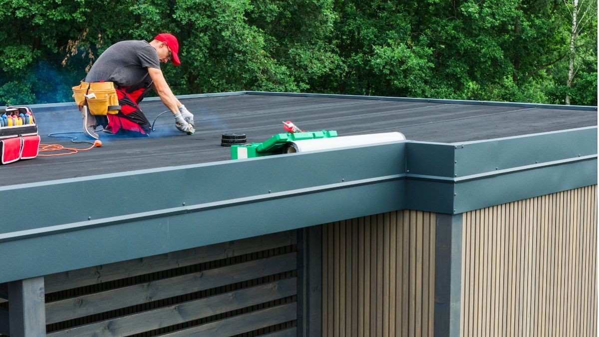Dakwerker plaatst EPDM dakbedekking op een plat dak van een bijgebouw, met professioneel gereedschap en metalen dakrand