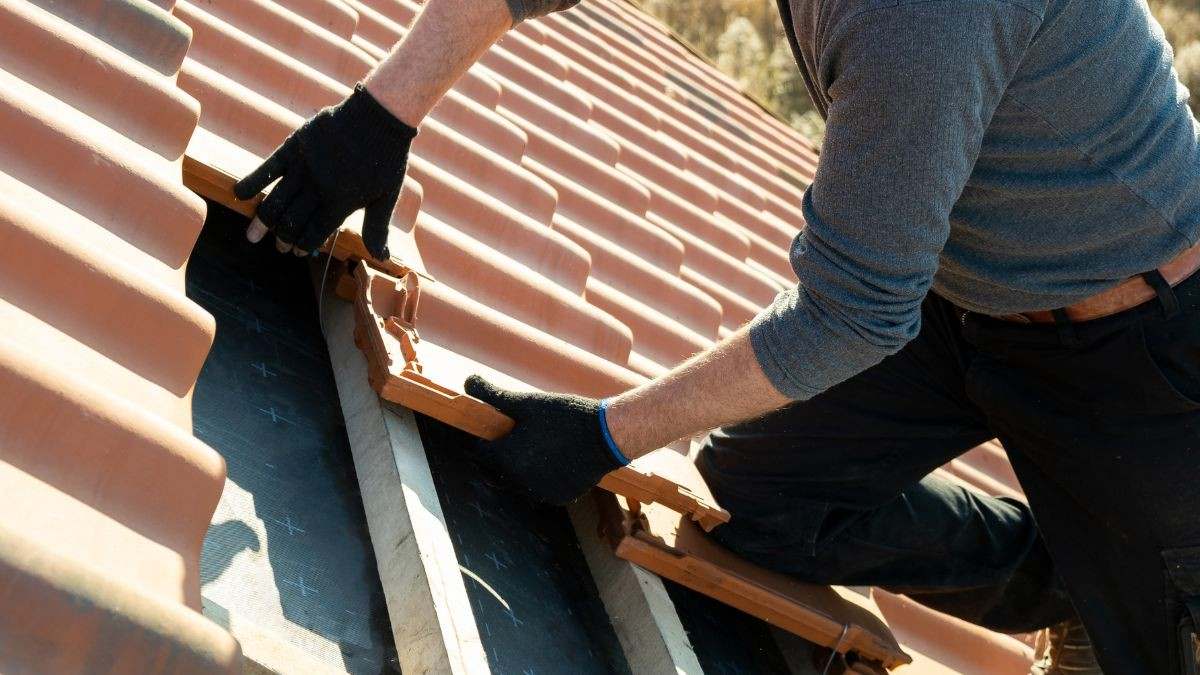 Vakman plaatst keramische dakpannen op houten panlatten boven een onderdakfolie bij de renovatie van een hellend dak