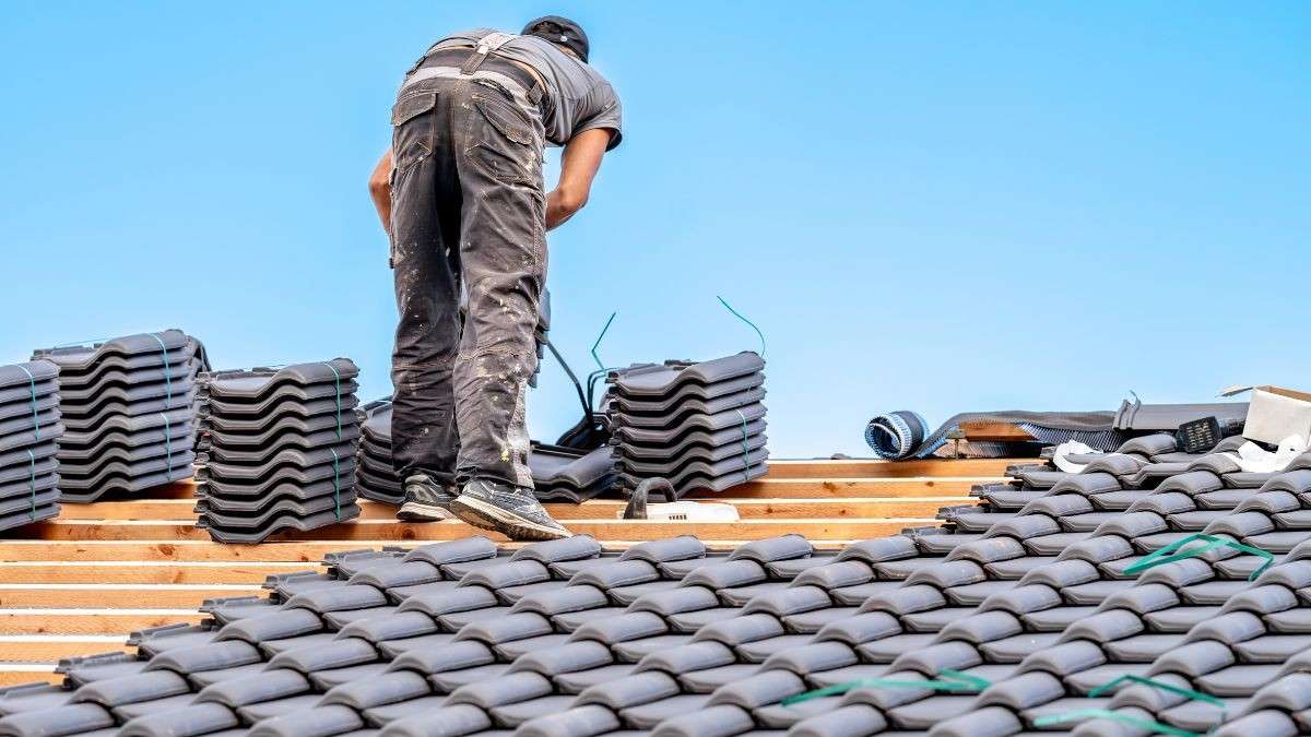 Dakwerker stapelt en legt antraciet stormpannen op houten panlatten bij de aanleg van een nieuw pannendak