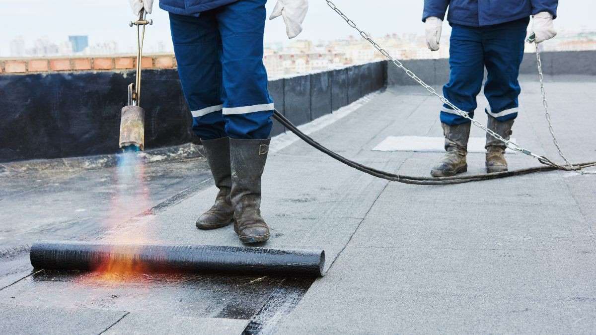 Twee dakwerkers branden een rol bitumen roofing op een plat dak tijdens een professionele dakherstelling