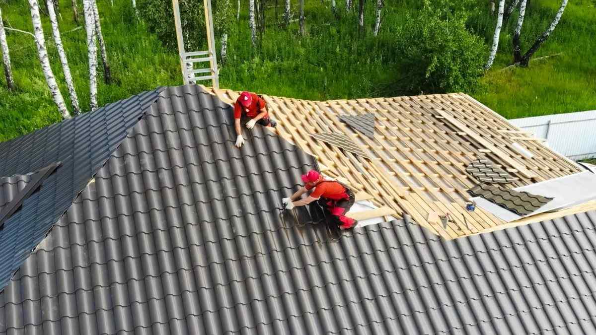 Twee dakwerkers plaatsen donkergrijze holle dakpannen op een hellend dak met zichtbare panlatten en onderdakfolie