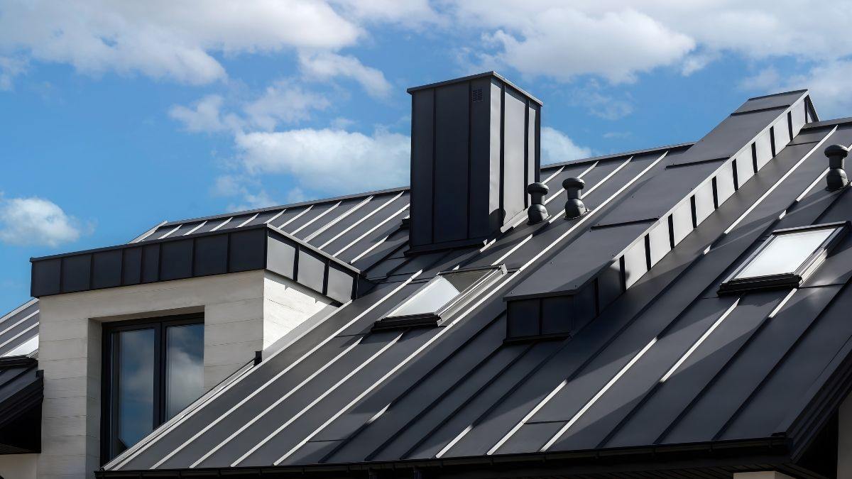 Antraciet gekleurd dak van zink met staande naad op een moderne woning met schoorsteen en dakramen tegen blauwe lucht