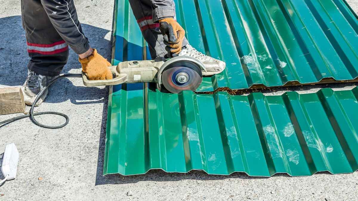 Dakwerker zaagt groene geprofileerde stalen dakplaten op maat met een slijpschijf voor de montage van het dak