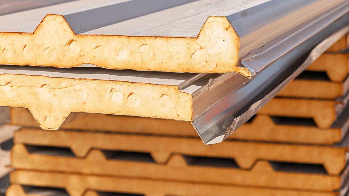 Gestapelde sandwich dakplaten met trapeziumprofiel en oranje PIR-isolatiekern klaar voor plaatsing op het dak