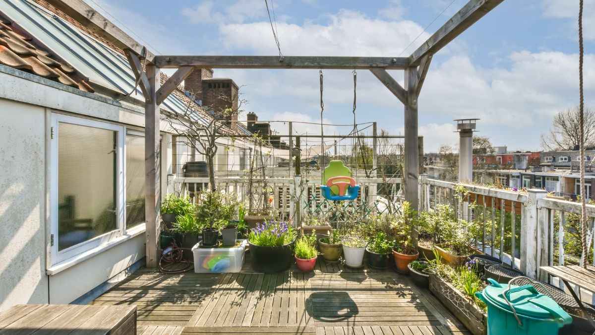 Groen terras vol plantenpotten en kruiden op een houten vlonder onder een verweerde pergola met klimplanten