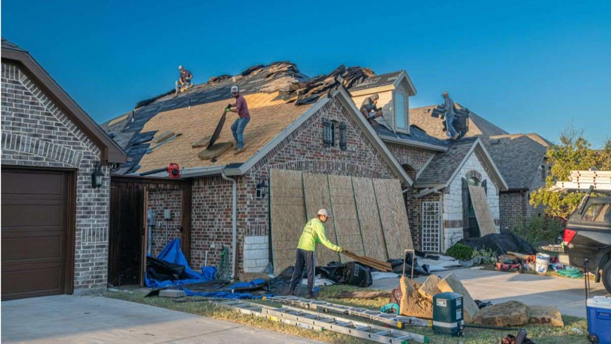 Meerdere dakwerkers verwijderen de oude dakbedekking van een bakstenen woning tijdens een volledige dakrenovatie