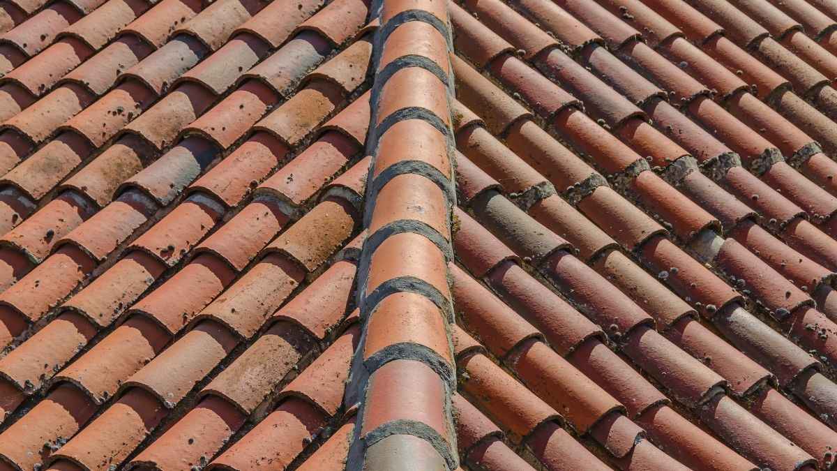 Twee dakvlakken bedekt met rode golvende keramische pannen, gescheiden door een gemetselde nokvorst op een hellend dak