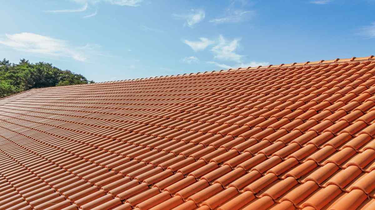 Hellend dak volledig bedekt met rode keramische kleidakpannen van Koramic tegen een strakblauwe lucht op een zonnige dag