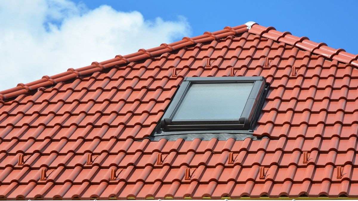 Hellend dak bedekt met rode keramische dakpannen en een geïntegreerd dakraam, met zichtbare nokvorsten onder een blauwe hemel