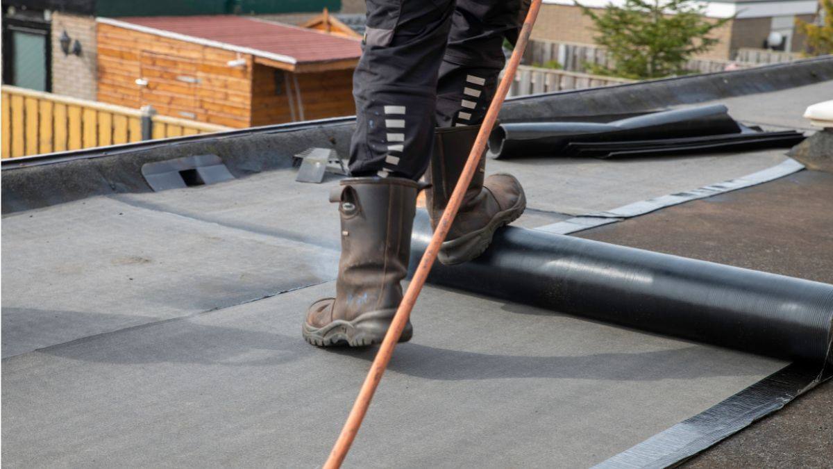 Vakman rolt nieuwe bitumen dakbedekking uit op een plat dak met rollen roofing en gasbrander op de achtergrond