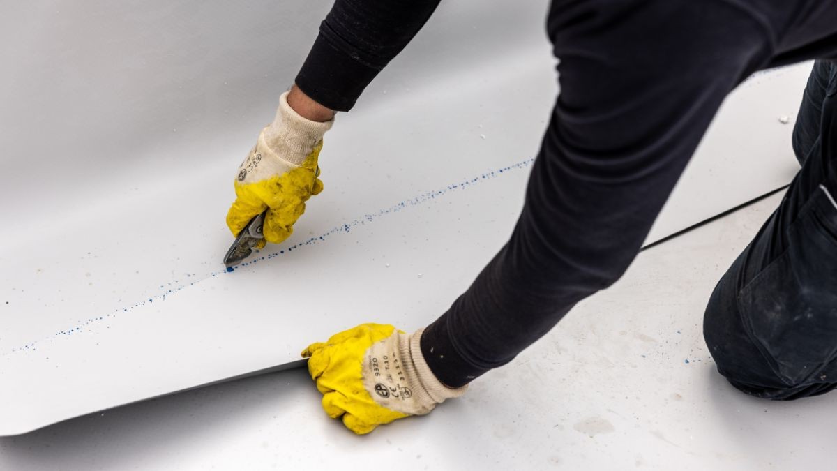 Dakwerker met beschermende handschoenen snijdt kunststof dakfolie op maat met een stanleymes voor een strakke afwerking