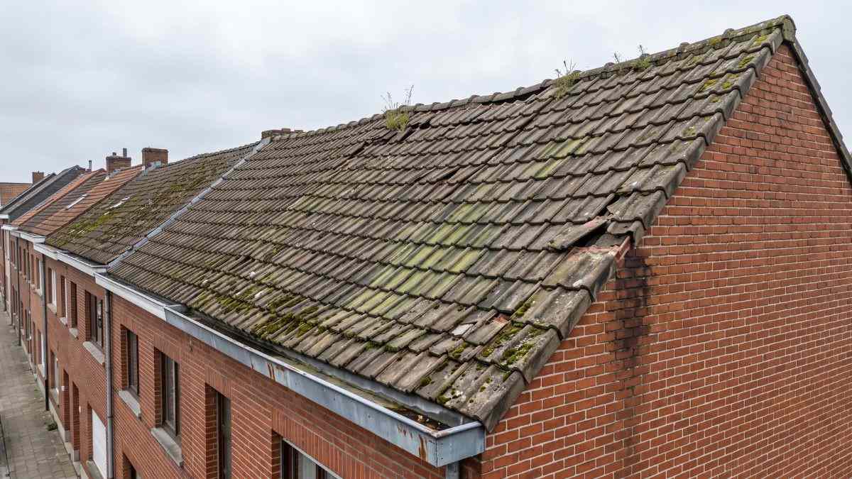 Verweerd pannendak met mosgroei en verschoven dakpannen op een Belgische rijwoning die toe is aan dakrenovatie