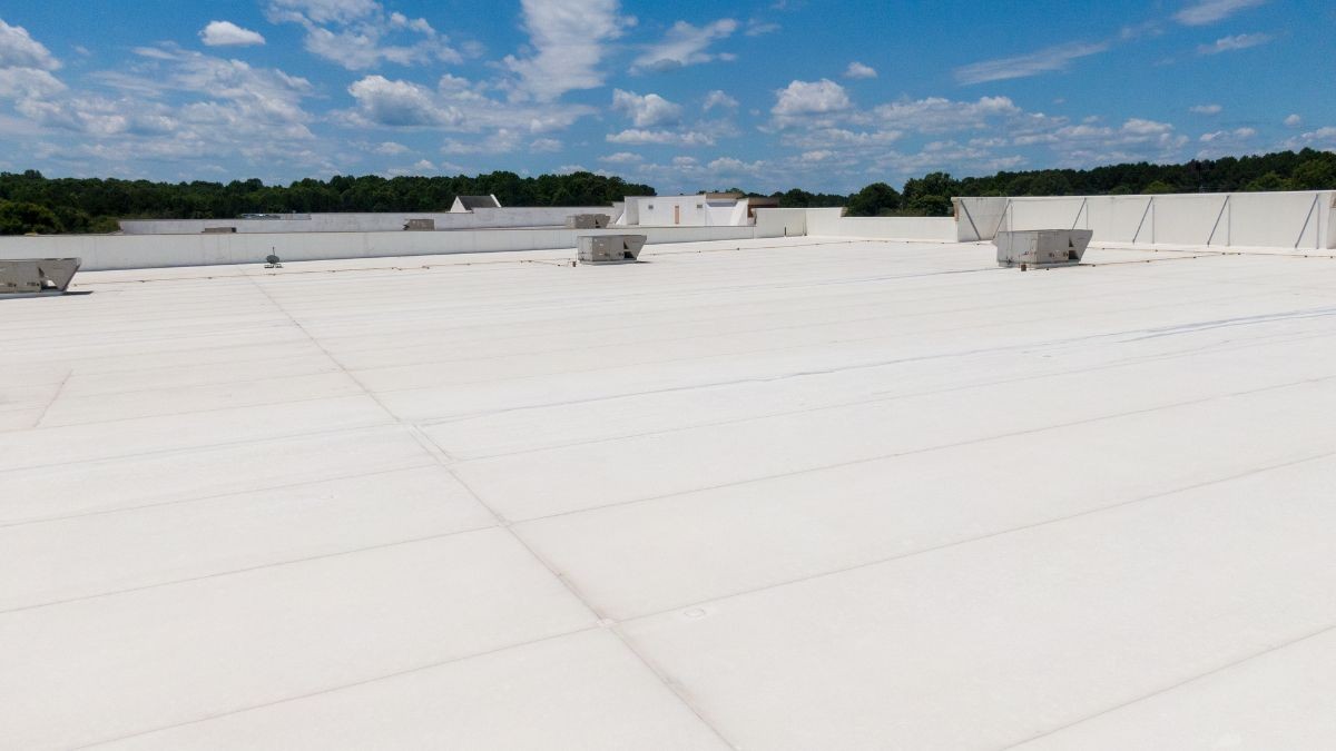Groot industrieel plat dak afgewerkt met witte kunststof dakbedekking en zichtbare dakinstallaties onder blauwe lucht