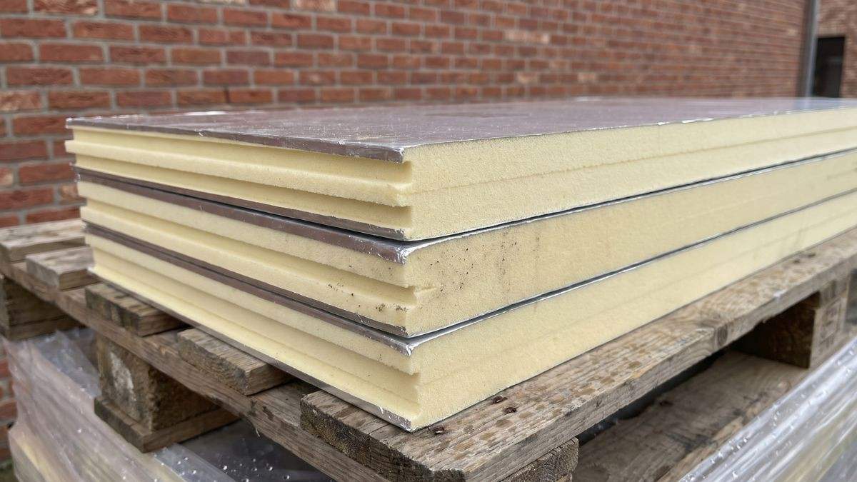 Met aluminium gecacheerde isolatieplaten met verspringende randen, gestapeld op een houten pallet tegen een bakstenen muur