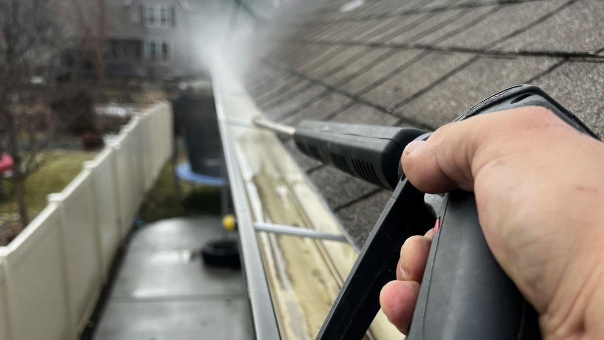 Vakman spoelt met een waterstraal het laatste vuil door de goot richting de regenpijp van een woning met een hellend dak