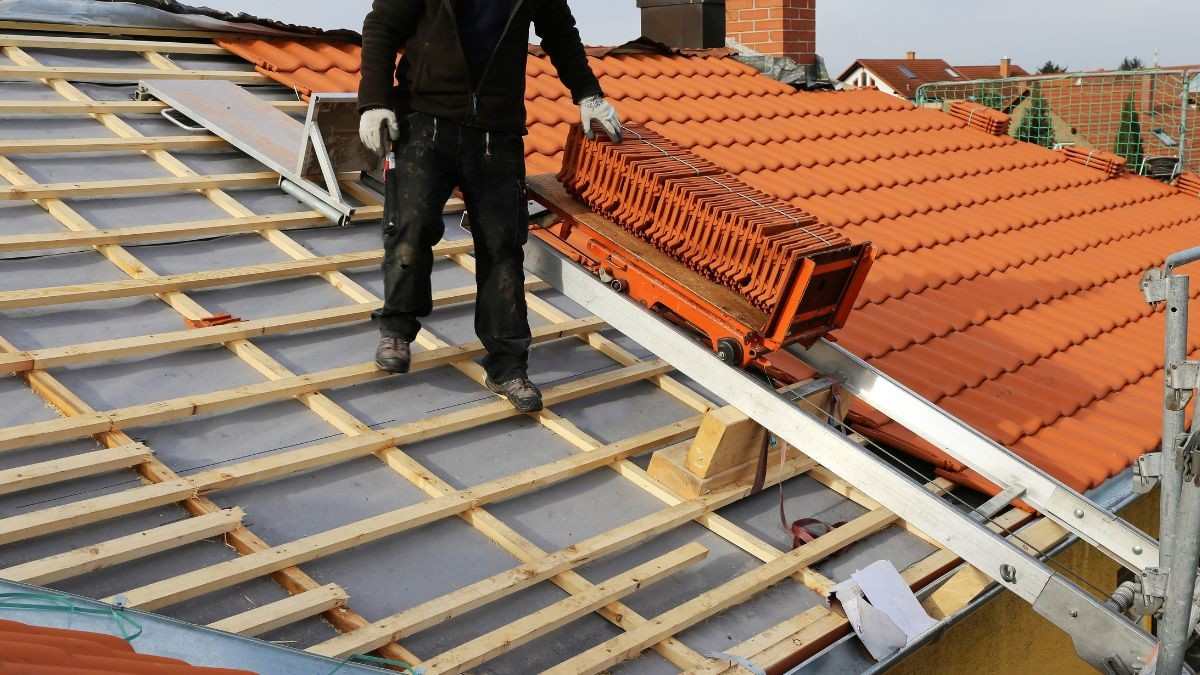 Dakwerker vernieuwt een schuin dak met nieuwe panlatten en onderdak, terwijl een dakpannenlift oranje dakpannen aanvoert