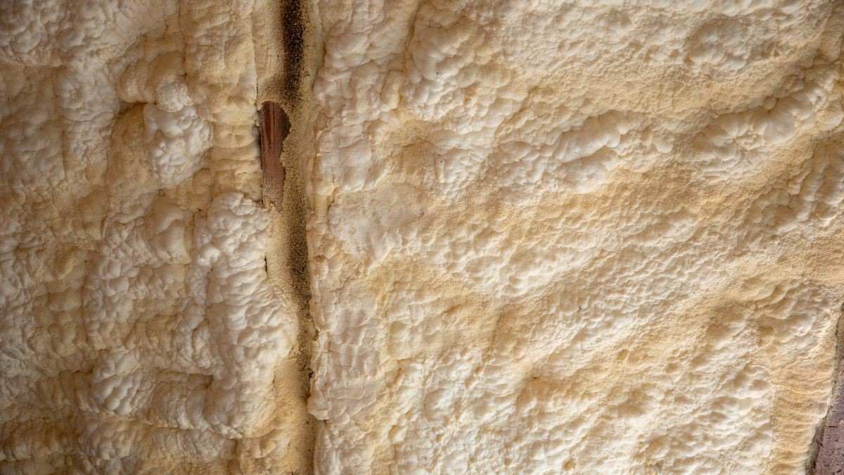 Detail van gespoten PUR dakisolatie waarbij het uitgeharde schuim naadloos aansluit tegen een houten keper