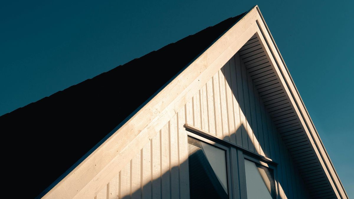 Witte houten gevelbekleding onder een donker hellend dak met overstek, gefotografeerd tegen een strakke blauwe lucht