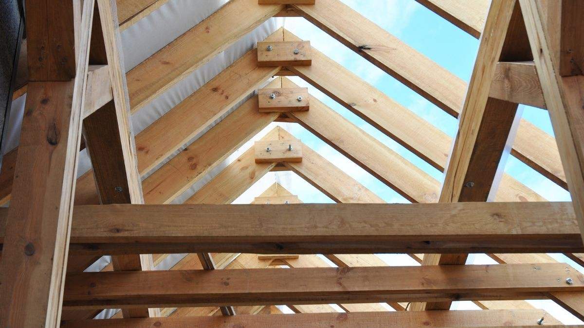 Zicht van onderuit op een houten dakgebinte met schuine kepers, verbonden aan de nok, en horizontale balken boven de zolder