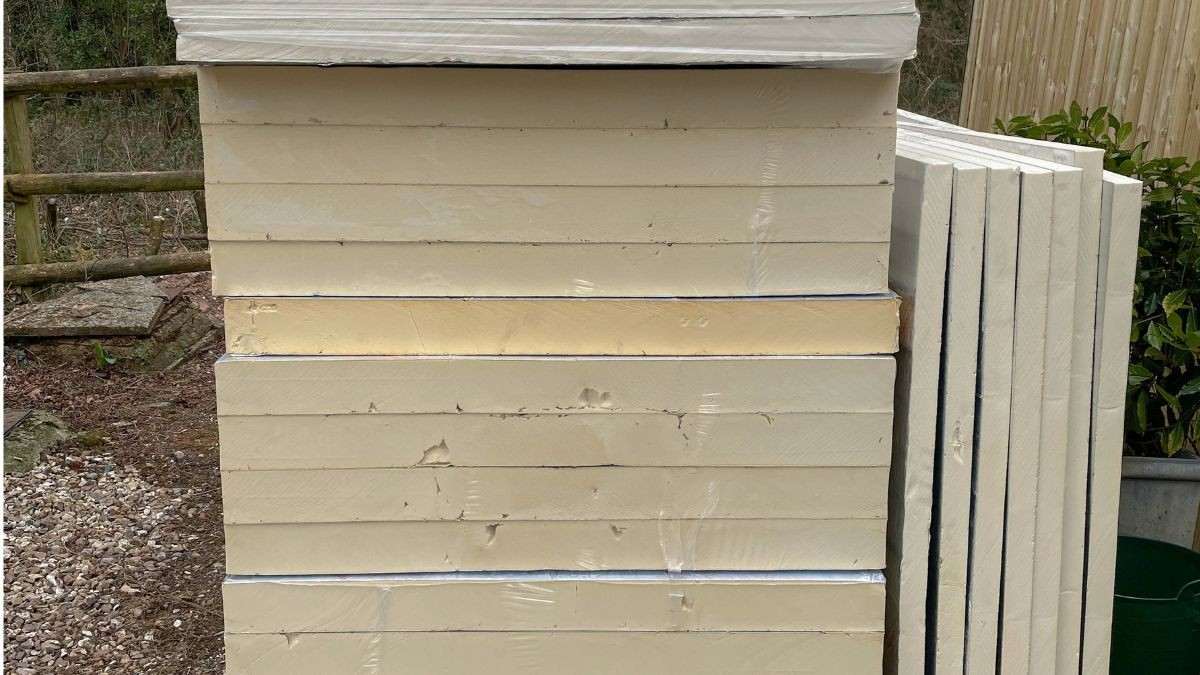 Gestapelde PIR-isolatieplaten met crèmekleurige kern buiten bij een woning, klaar voor gebruik als dakisolatie