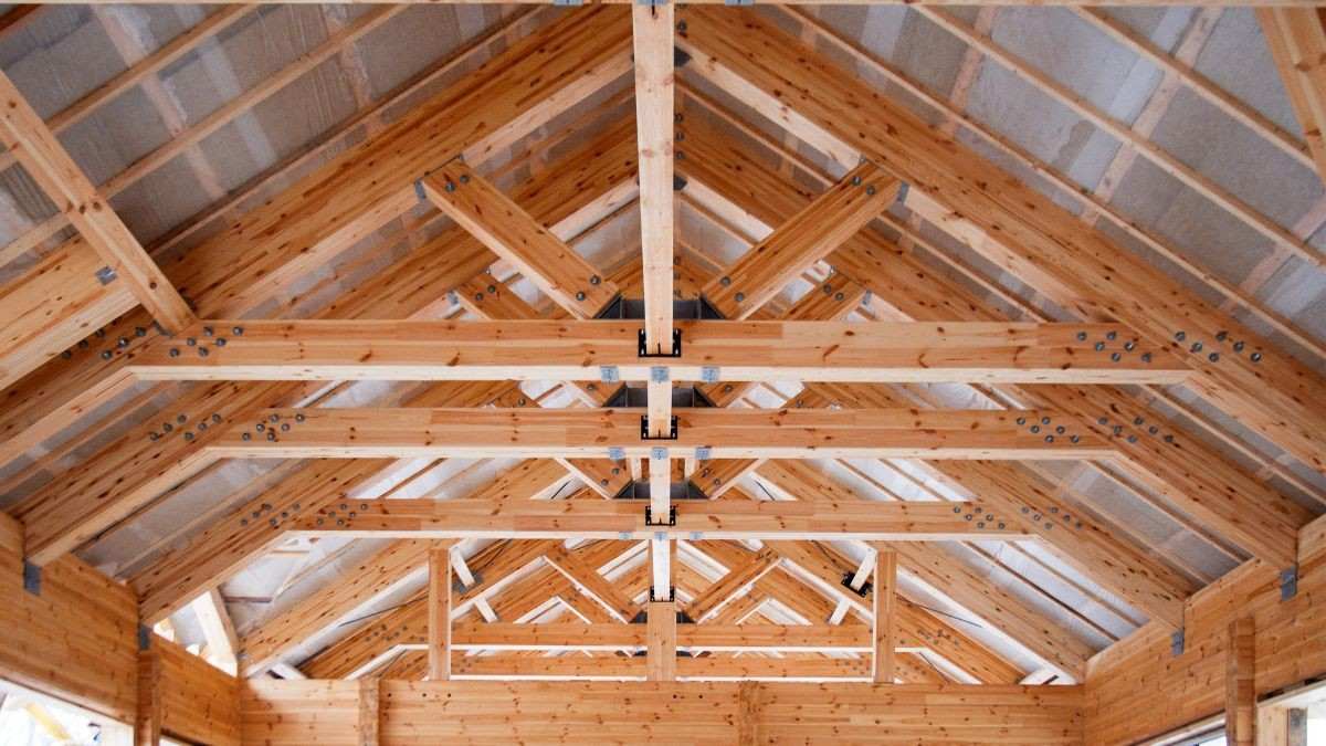 Een prefab spant voor een spantendak hangt aan een kraan en wordt door een dakwerker op de muren van de woning geplaatst.