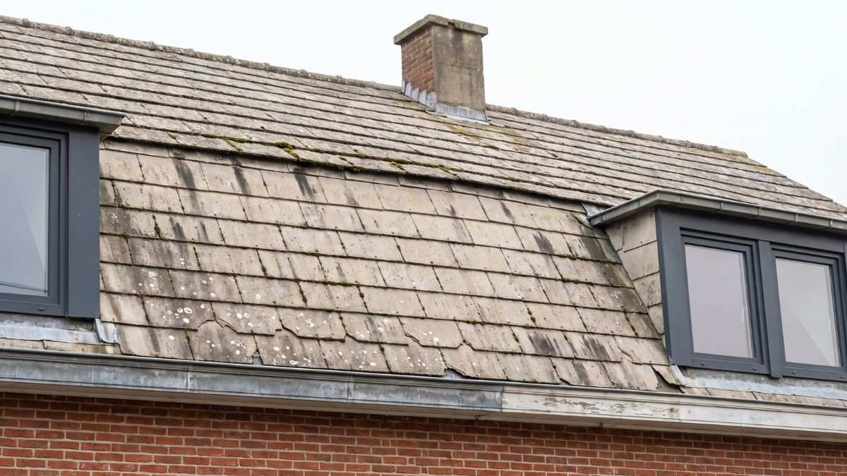 Woning met een verweerd dak van grijze kunstleien vol mos en witte vlekken, vlak voor de vervanging door asbestverwijderaars